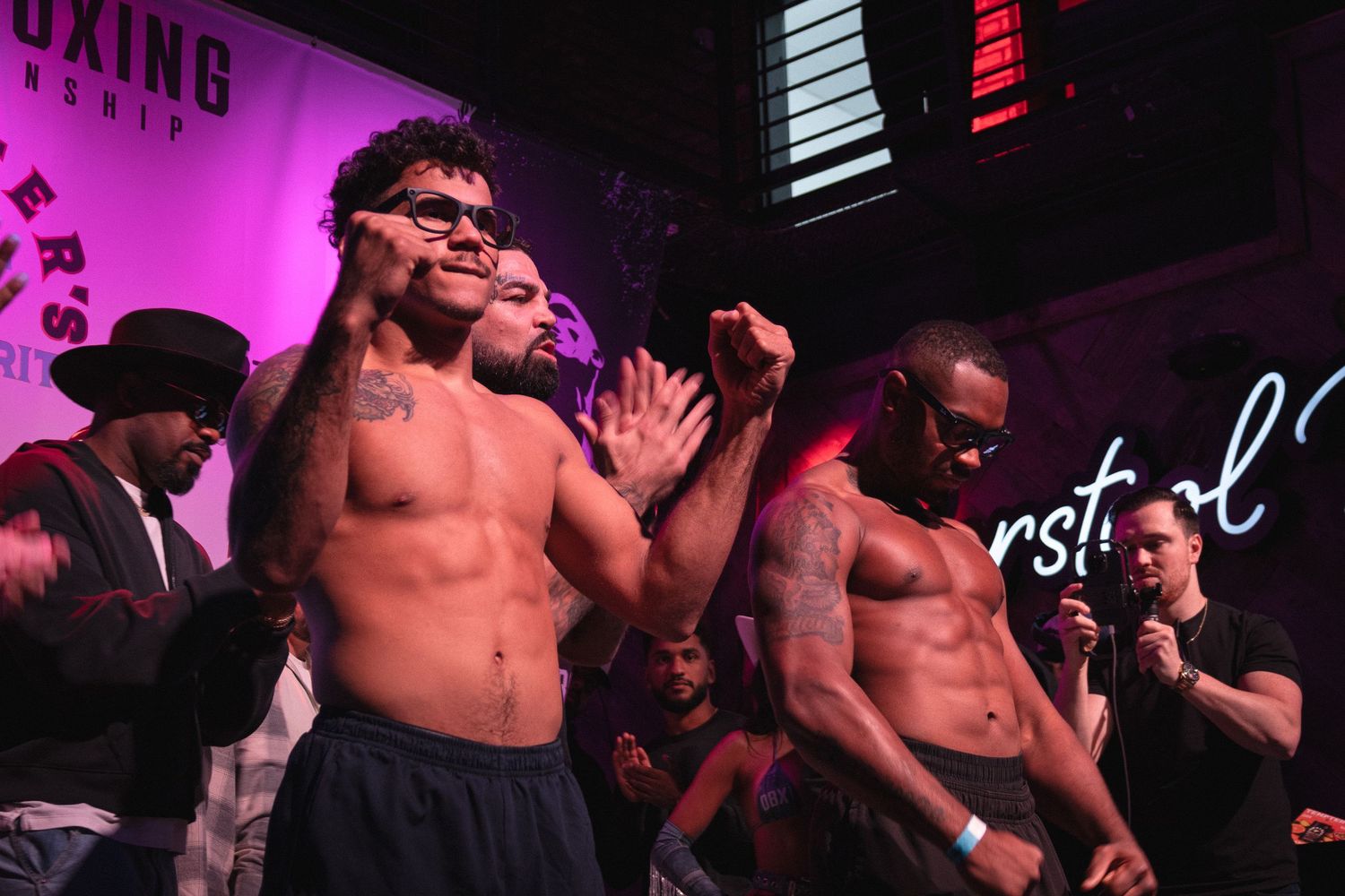 Shirtless performers energetically entertain on stage under purple lighting at a nightclub venue.