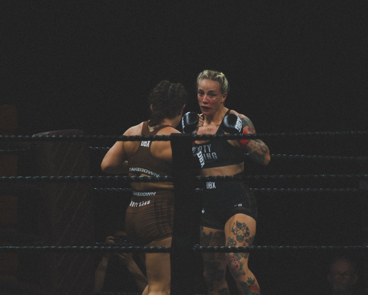 Athletes engage in close-quarters combat during a boxing match on a dark stage.