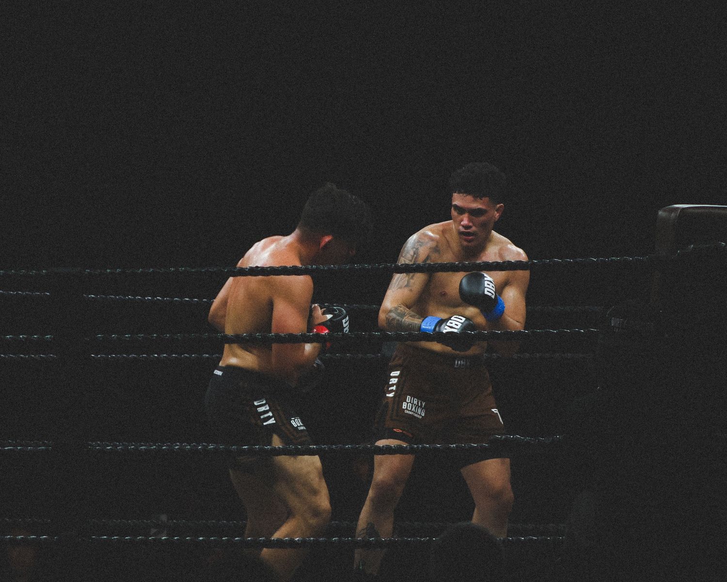 Two athletes trade blows in a professional boxing ring under dramatic lighting.