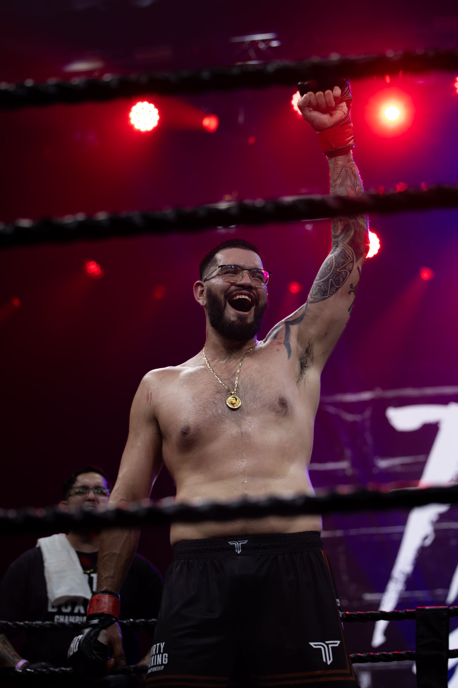 A shirtless boxer raises his arms in victory under red stage lighting.
