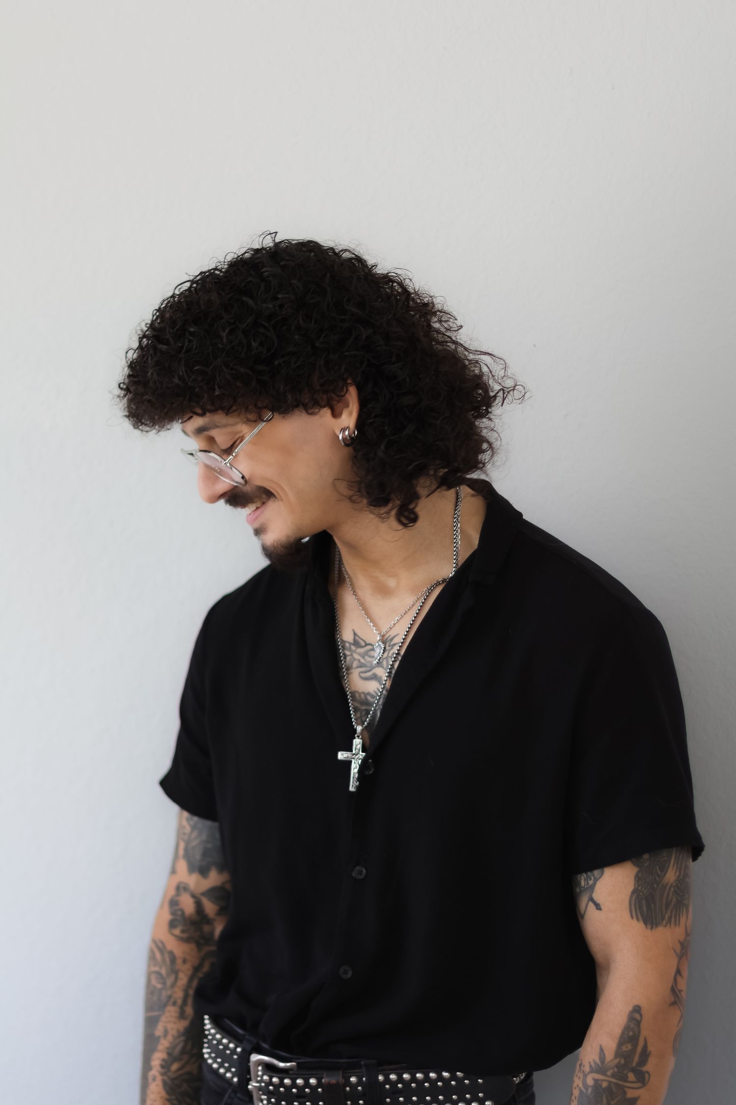 A person wearing a black shirt and cross necklace poses against a white backdrop.