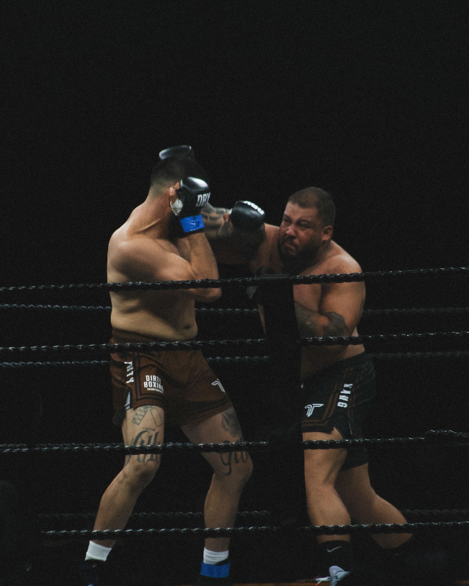 Boxers exchange powerful strikes in a dimly lit professional boxing ring.