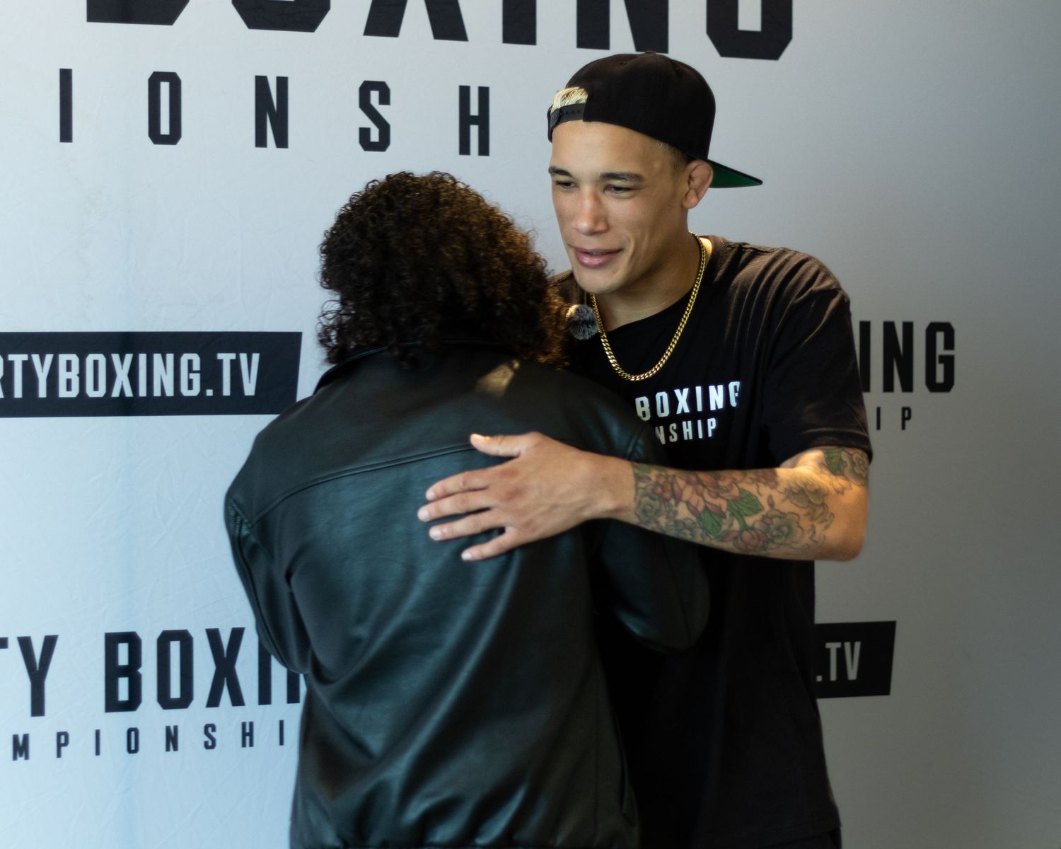 Two athletes share a friendly embrace at a boxing promotional event.
