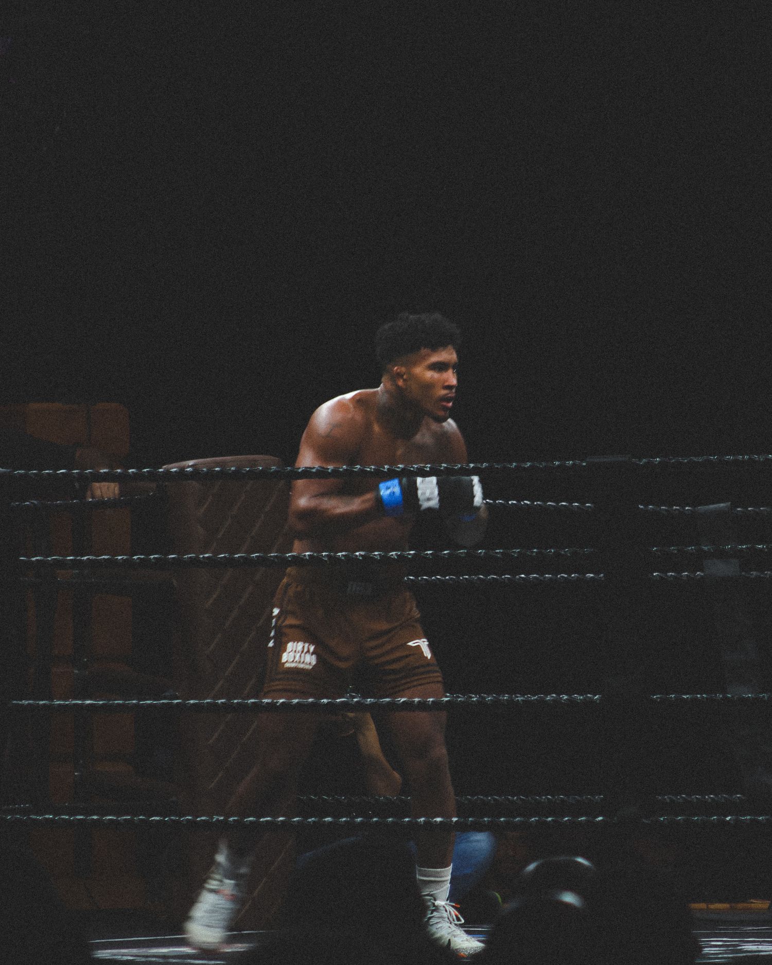 A boxer in brown shorts throws a powerful punch during a competitive match.