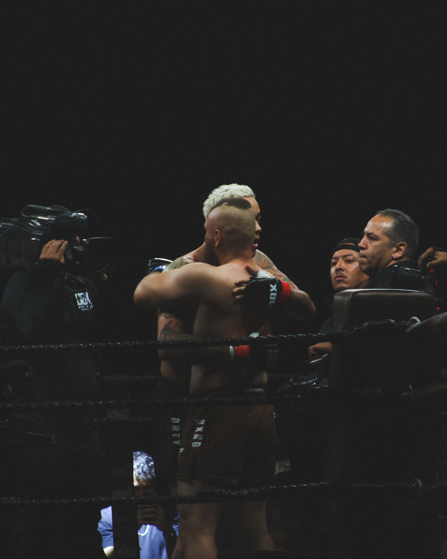 Two fighters trade blows during a professional boxing match under dramatic lighting.