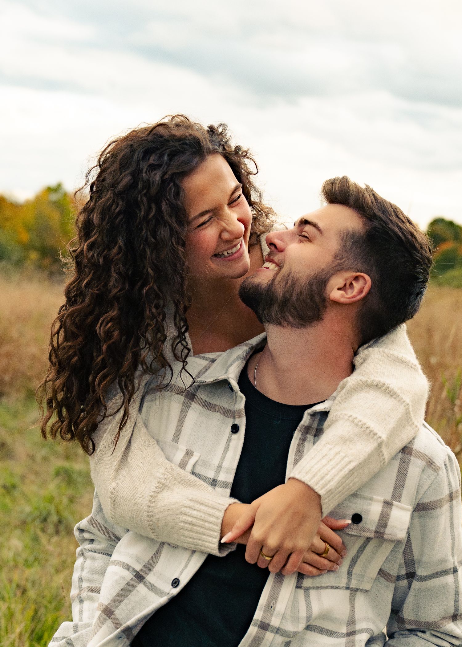 A couple shares a playful and affectionate moment together in a sunlit autumn field.