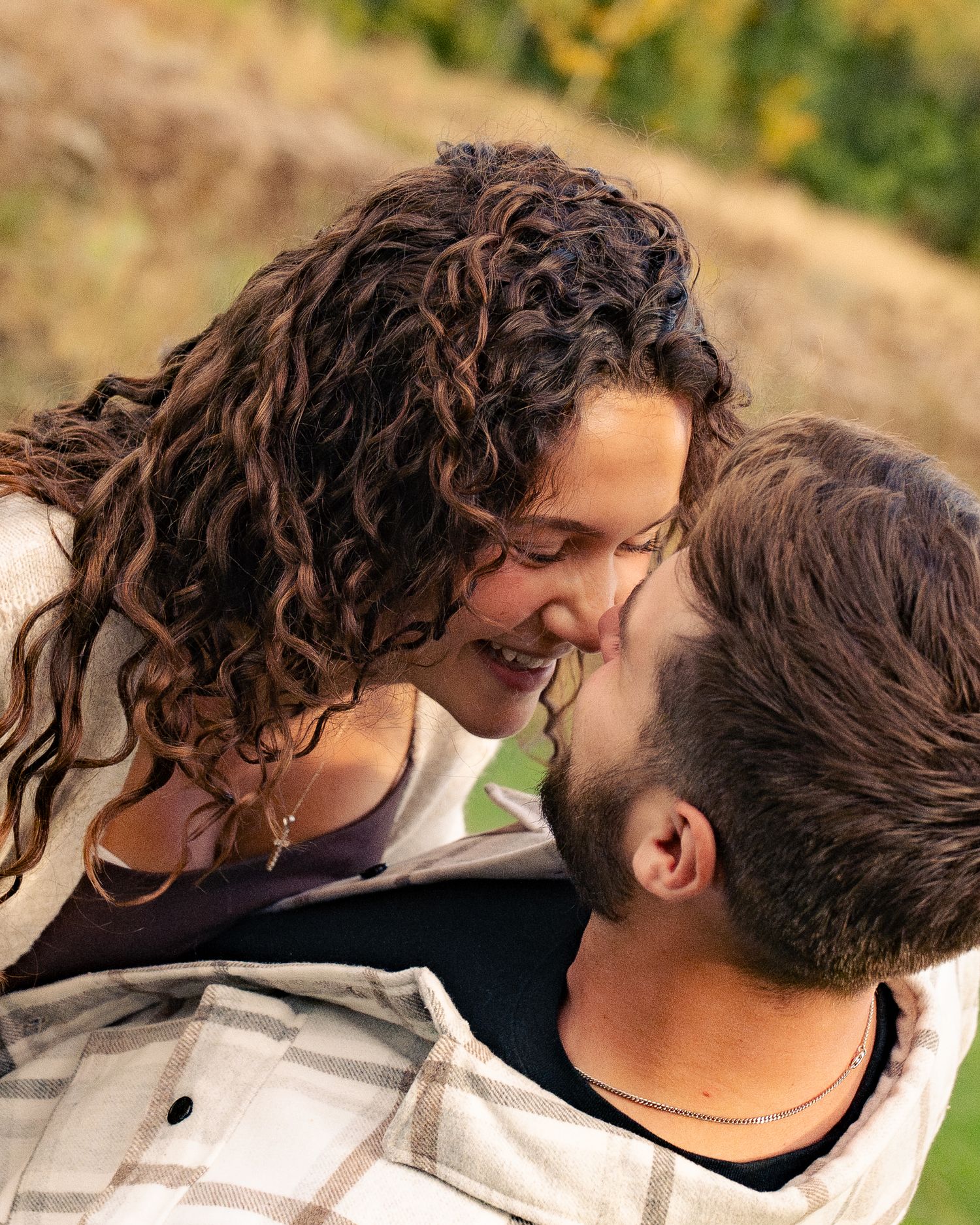Two people share an intimate moment outdoors with curly hair blowing in the breeze.