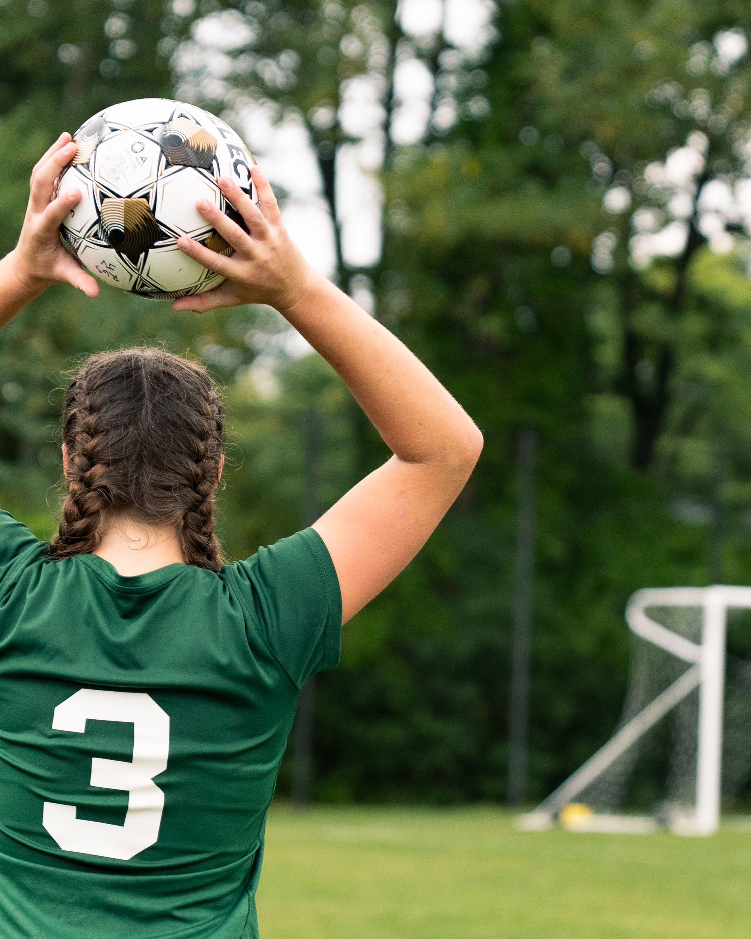 Soccer player in green jersey jumps up to catch ball during match on grassy field.