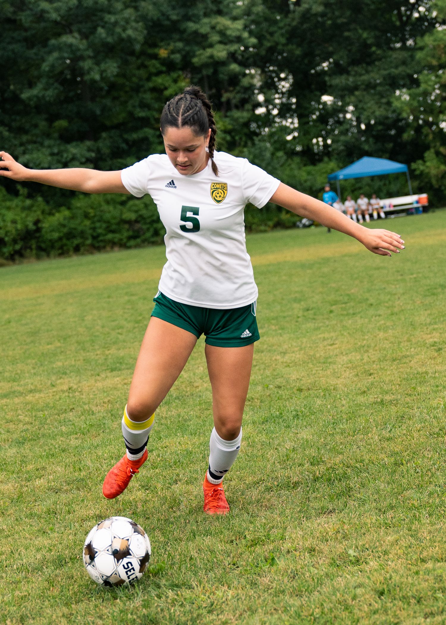 Soccer player in white jersey number 5 practices ball control on a grassy field during training.
