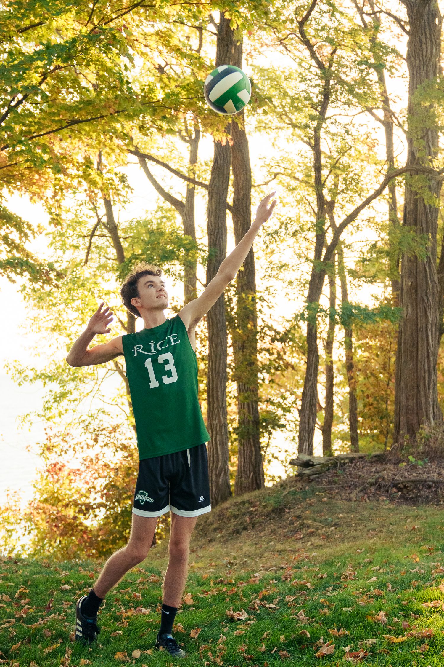 Volleyball player in green Rice University jersey performs serving sequence in wooded outdoor setting during fall season.