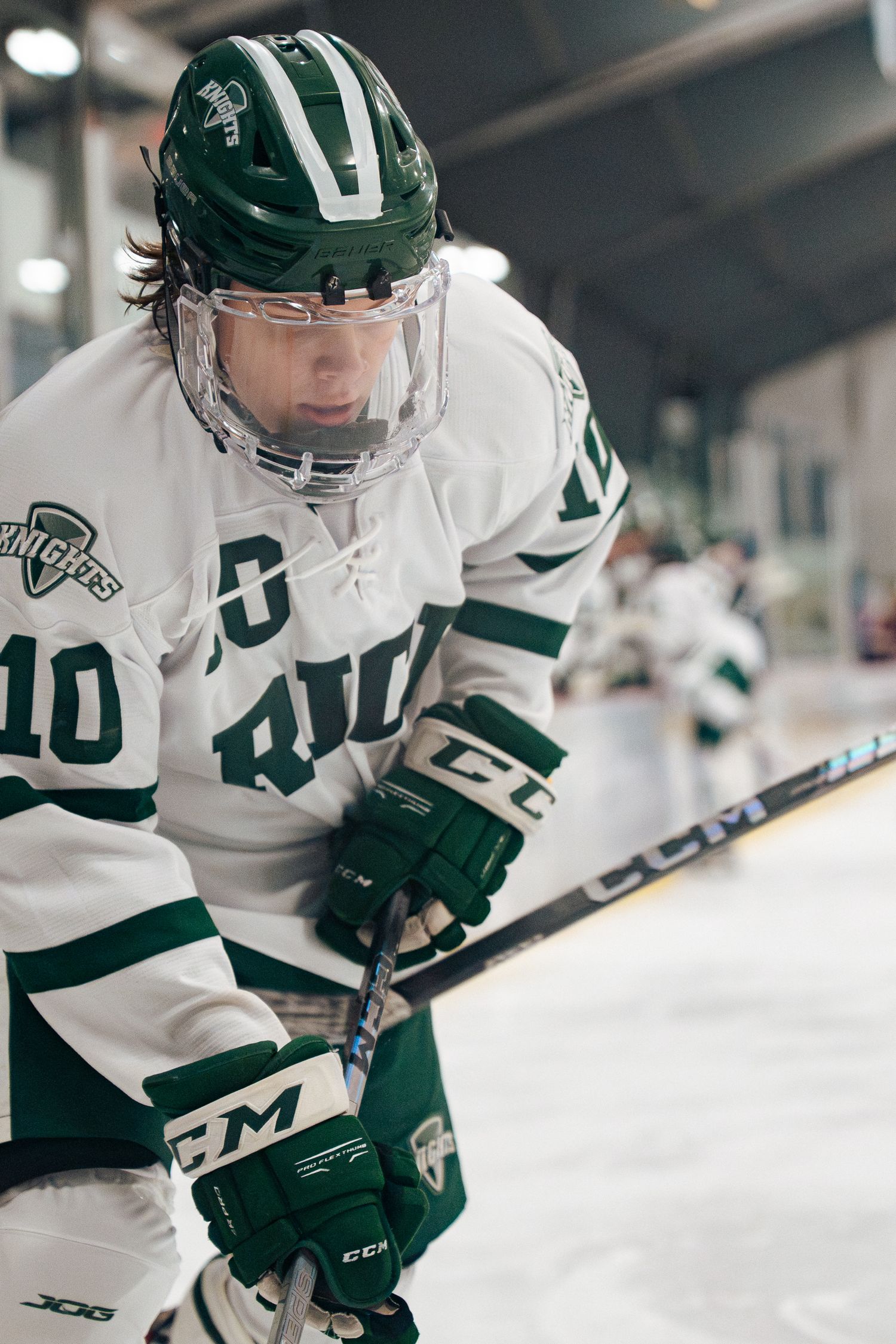 Hockey player in white jersey number 40 with green helmet and gloves leans forward during game.