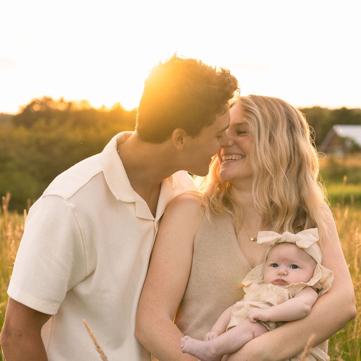 Parents cuddle with baby during outdoor sunset photo session.