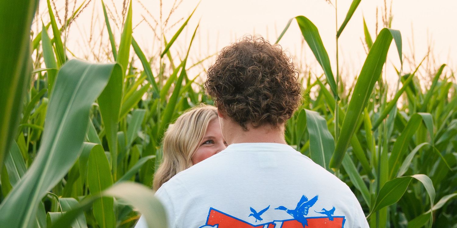 Romantic couple standing among tall green corn stalks at sunset.