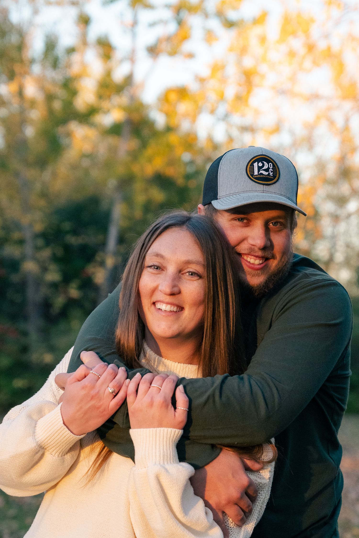 A couple shares playful moments together outdoors during a fall photoshoot with golden autumn trees in background.