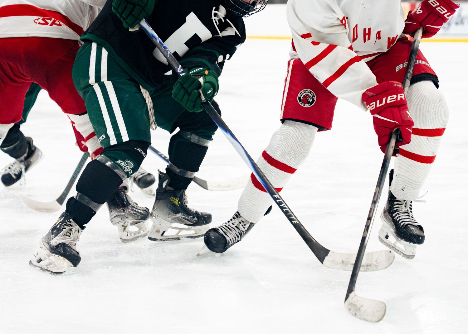 Ice hockey players in red and green jerseys battle for position during an intense game sequence.