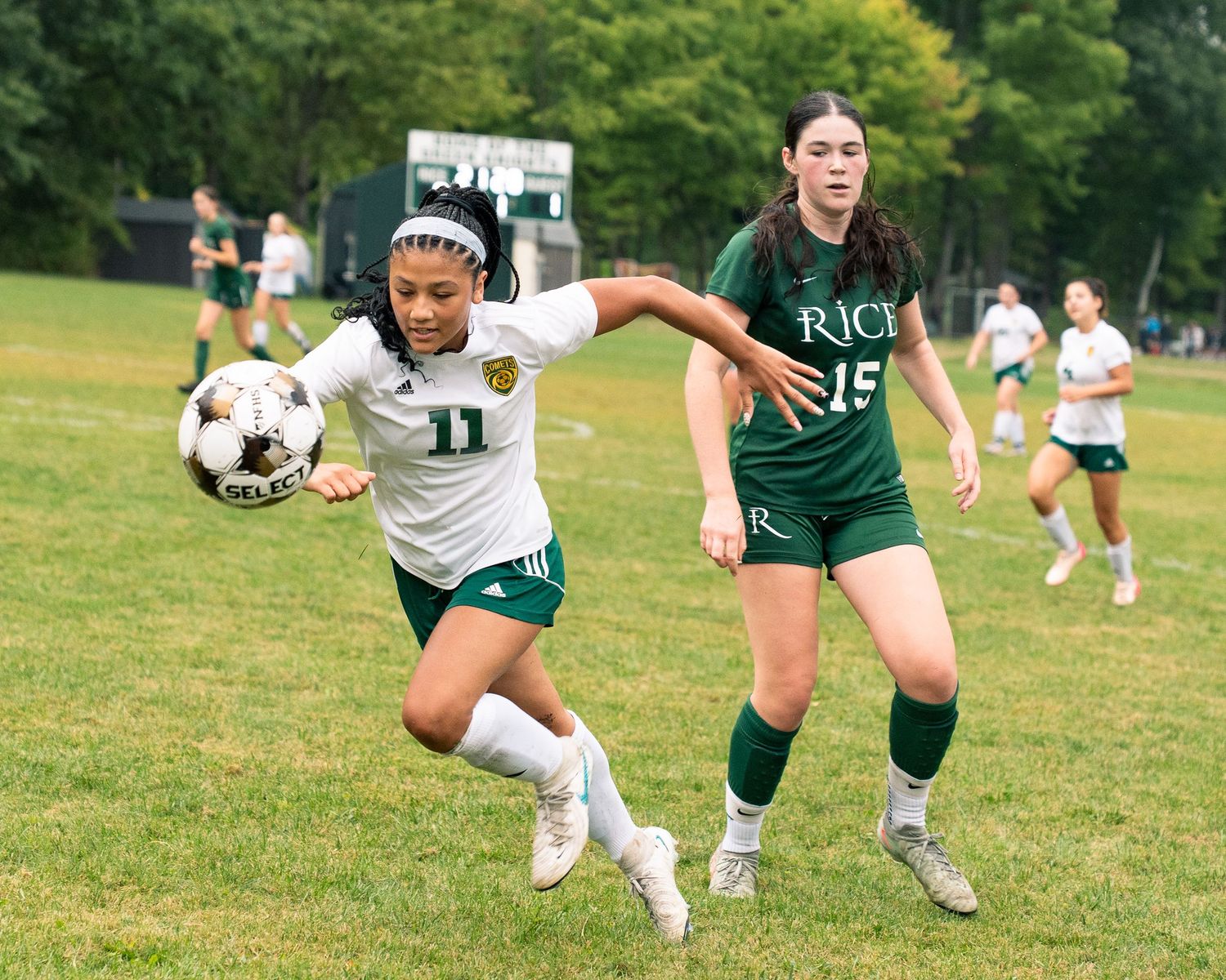 College women's rugby players competing in an outdoor match on a grass field during a summer day.