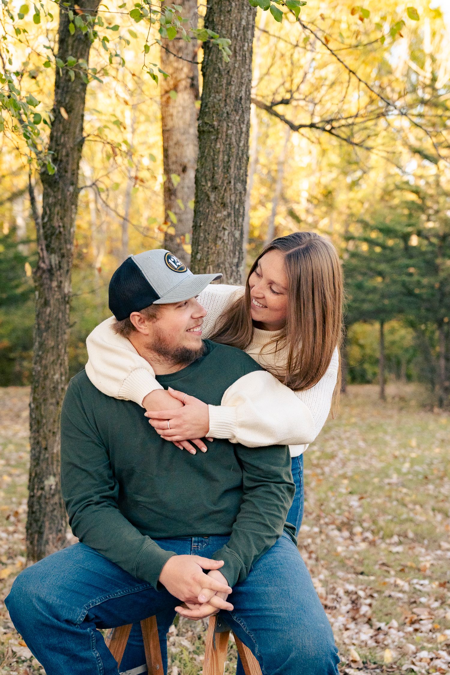 A couple shares tender moments while sitting outdoors among autumn trees and fallen leaves.