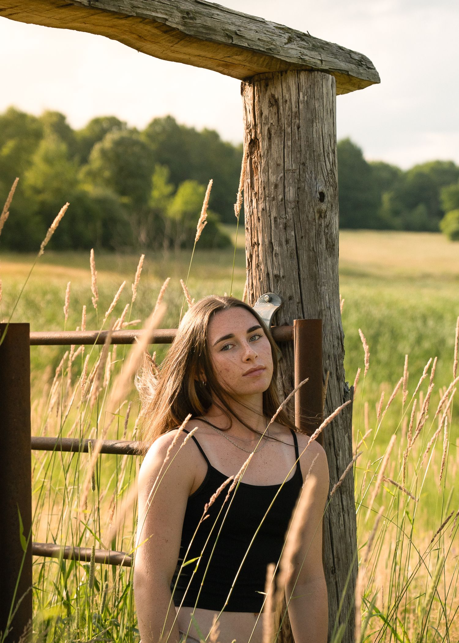 Summer portrait by a rustic wooden fence post surrounded by tall grass.