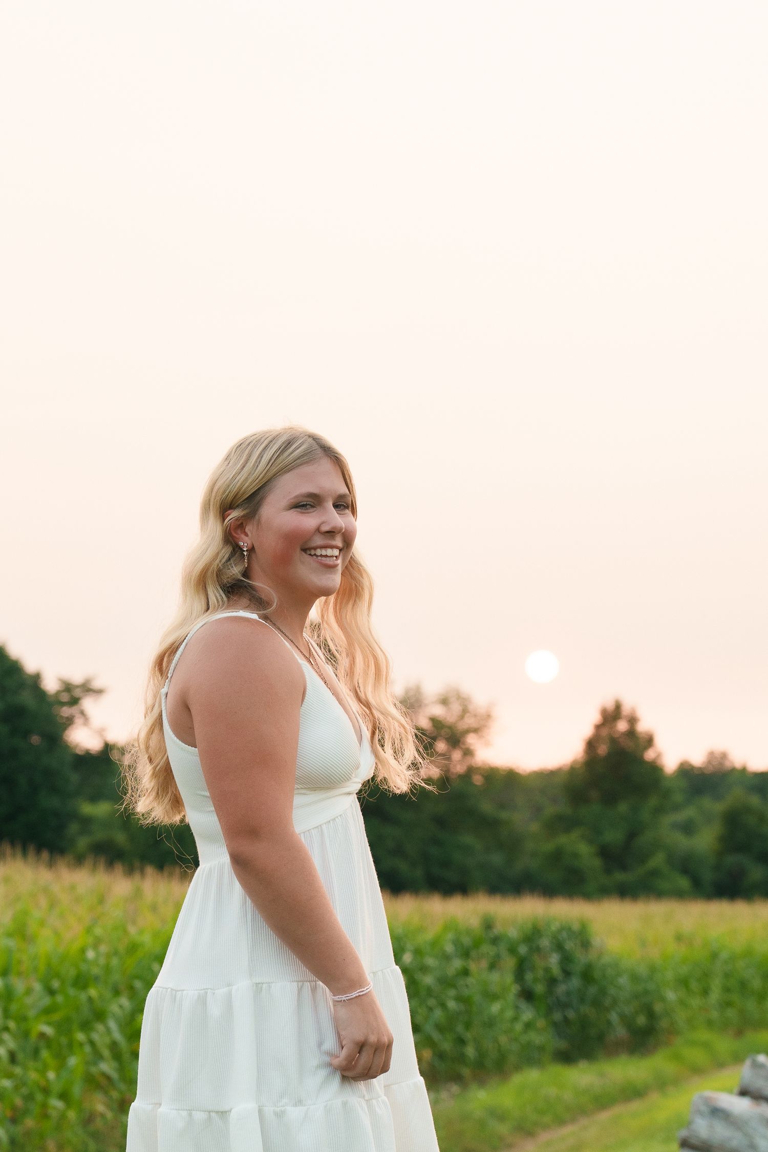 A person in white dress smiles during sunset in a grassy meadow.