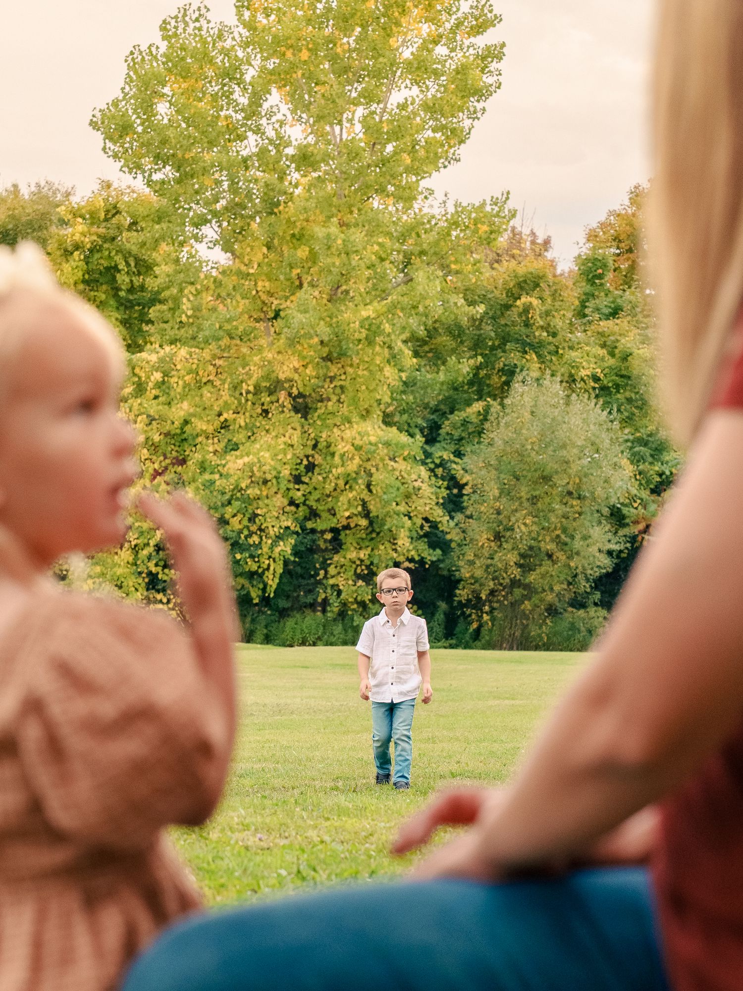 A child runs joyfully through a grassy field with autumn trees in the background on a sunny day.