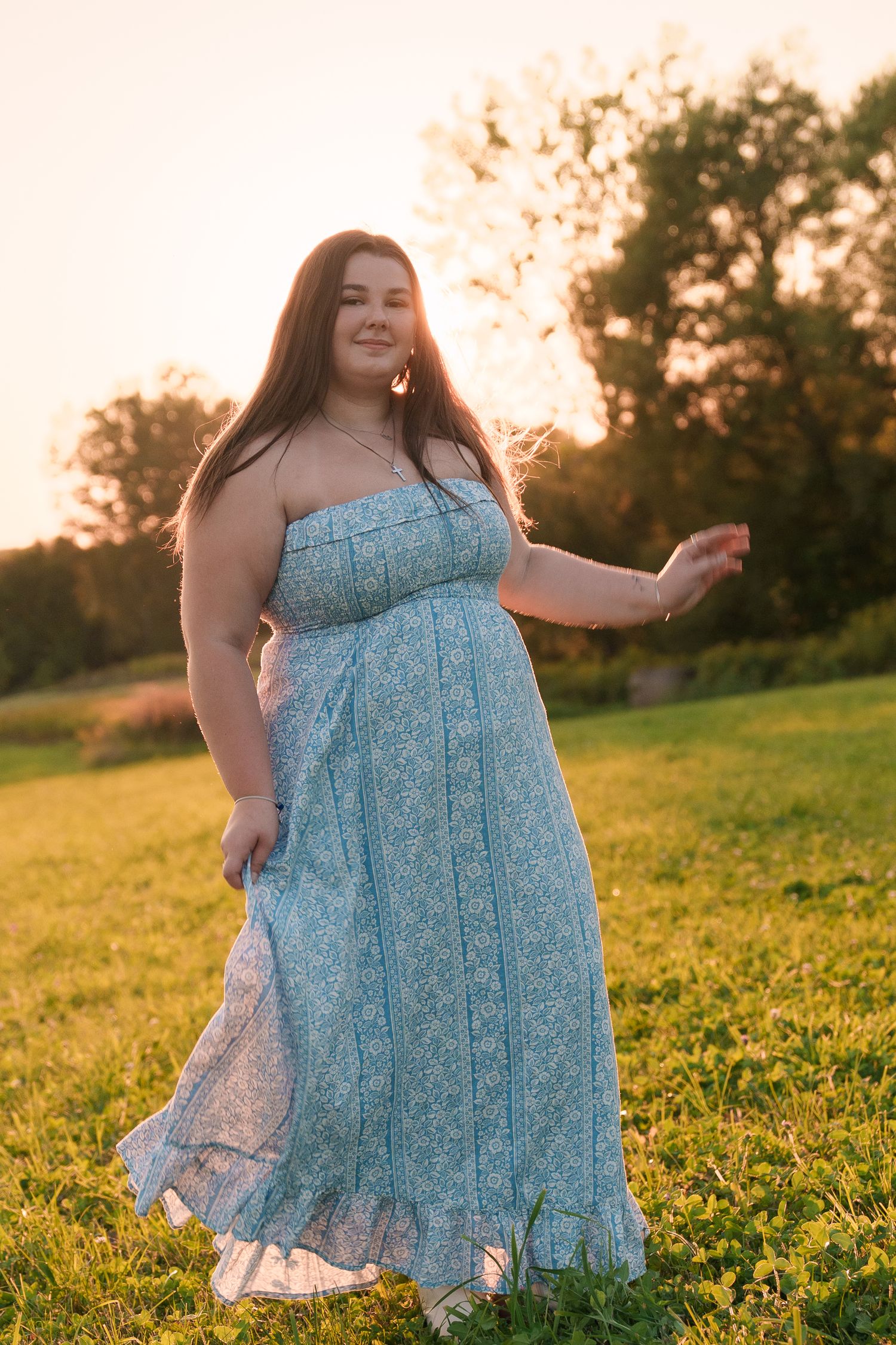 Person in a flowy blue floral dress twirls gracefully in a sunlit meadow during golden hour.