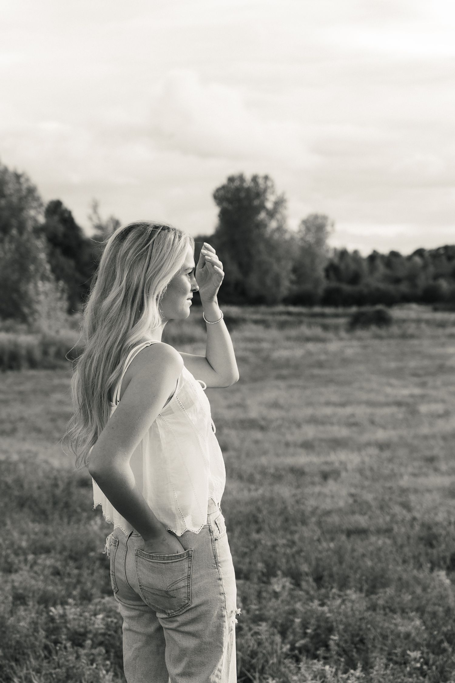 A series of monochromatic photos showing someone in a white top standing in a rural field on a cloudy day.