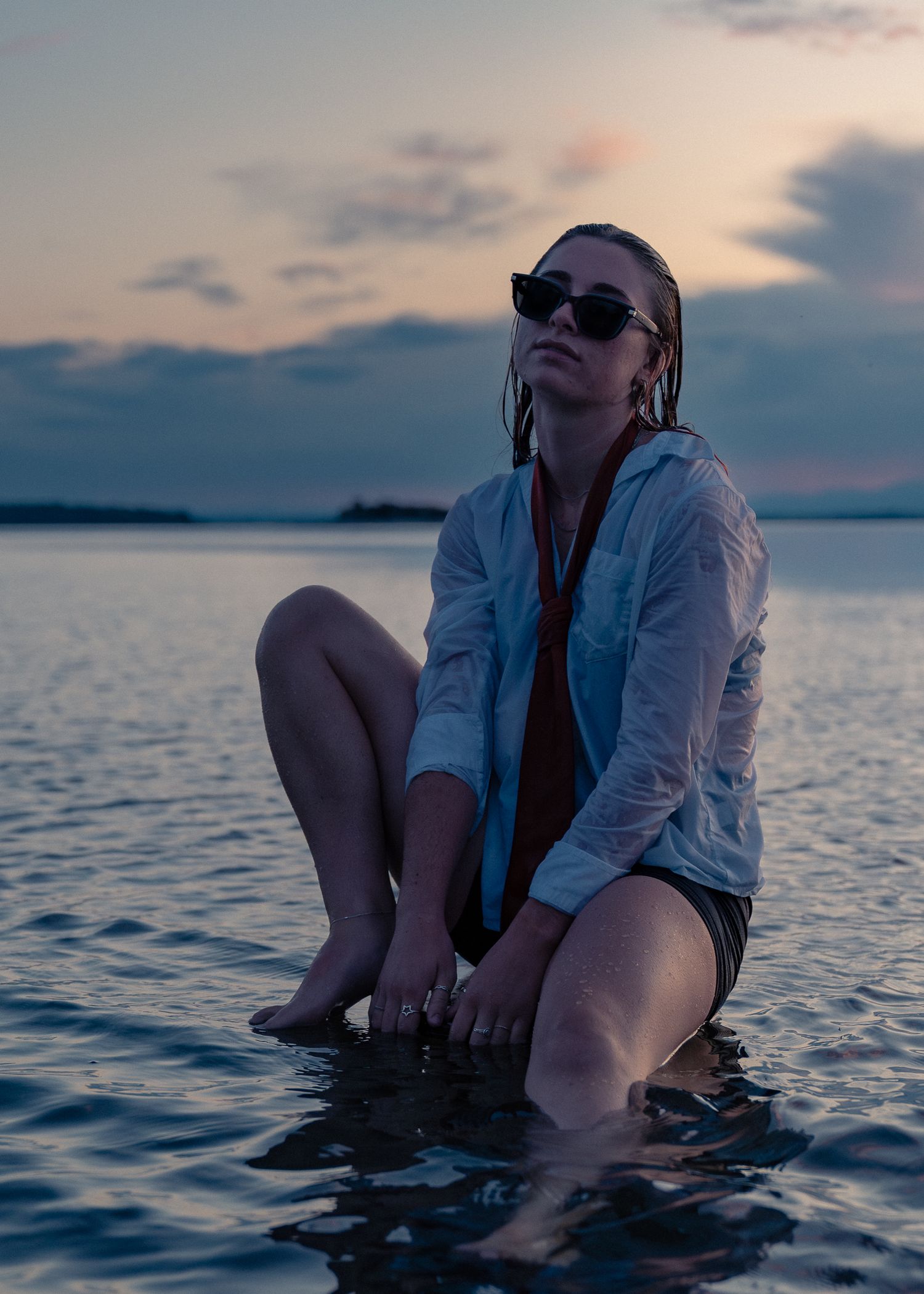 A person sits with their legs in calm ocean waters during sunset, creating a peaceful and serene atmosphere.