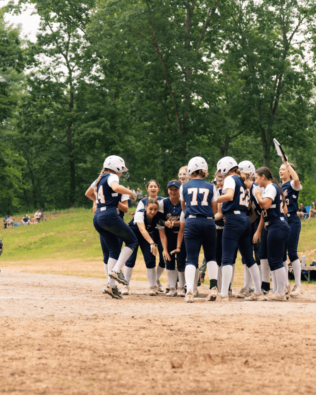 Softball team in navy uniforms gathered on a dirt field during practice.