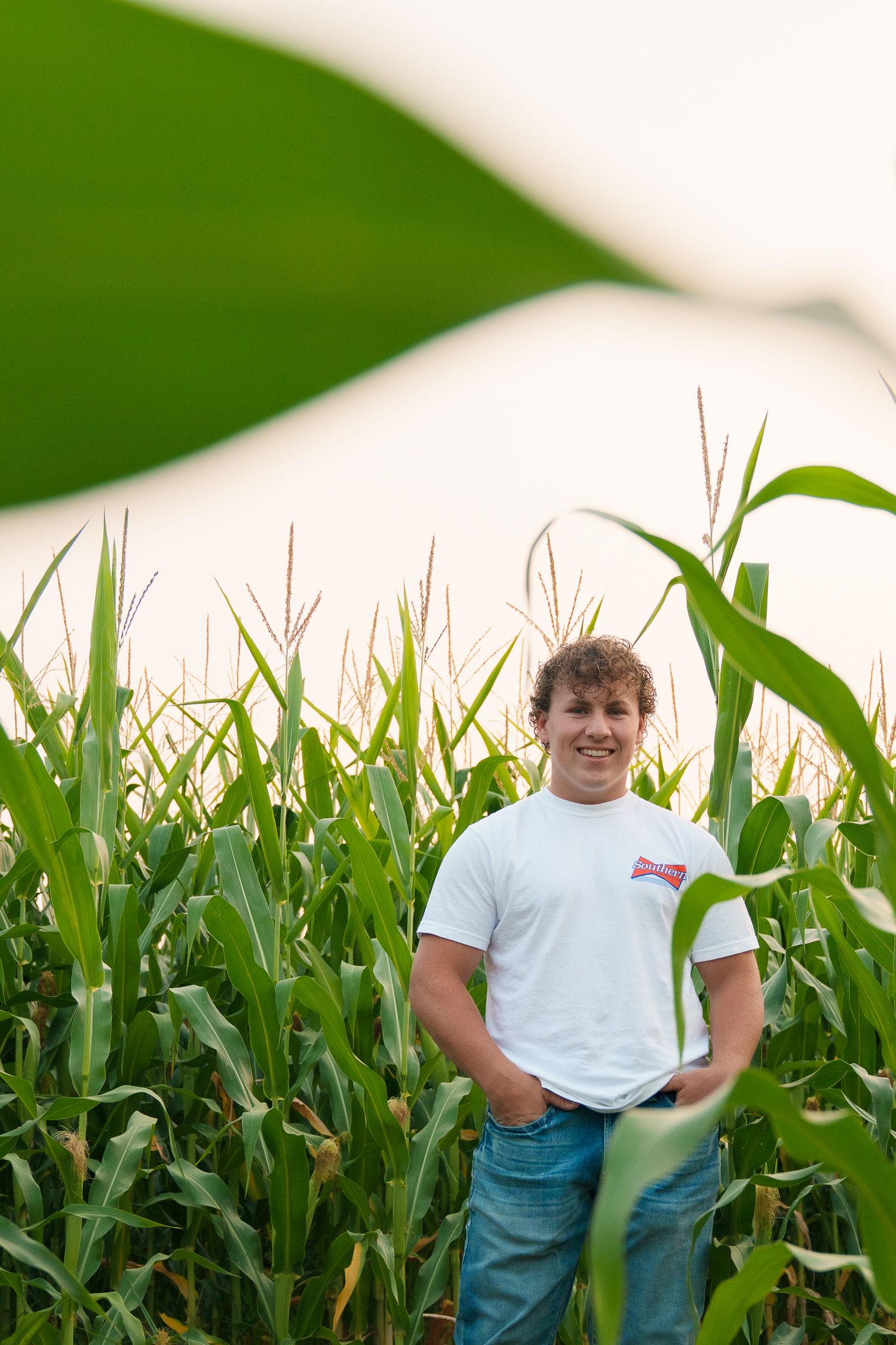 A casual portrait taken in a cornfield with person wearing white t-shirt against green stalks.