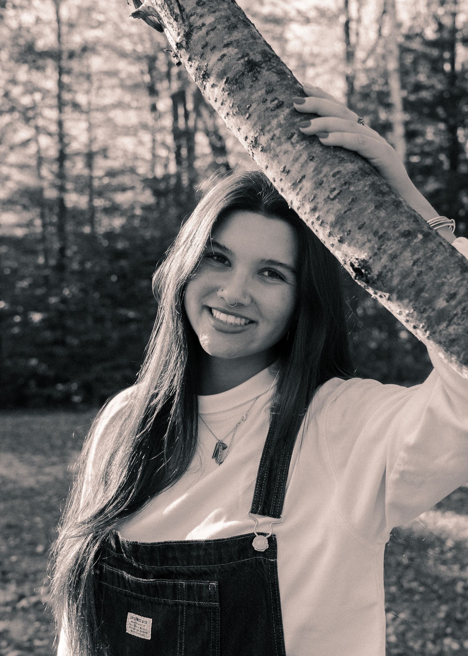A series of black and white portraits showing a person in overalls posing next to a tree trunk in a forest setting.