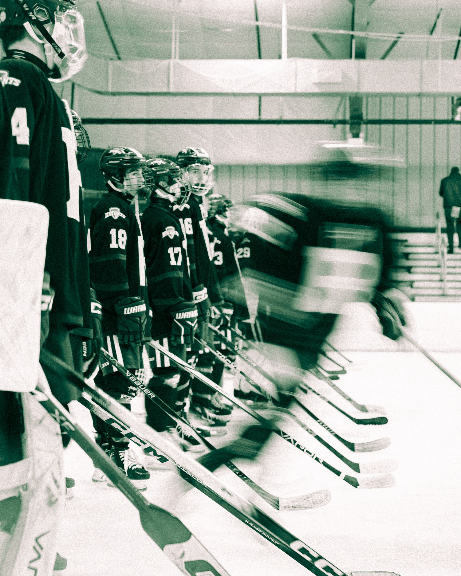 Motion blur captures hockey players lined up along the boards during a game in black and white vintage photograph.