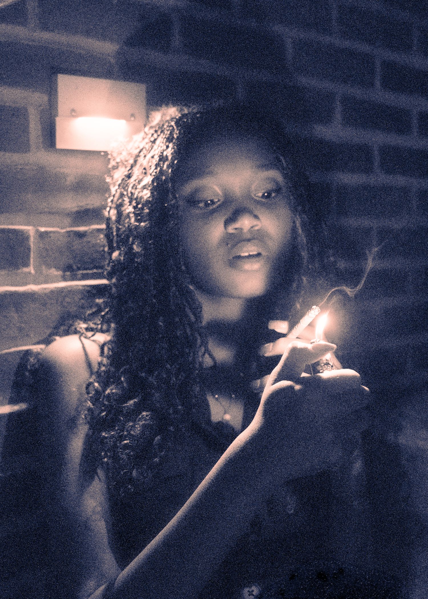 Artistic low-light portrait with dramatic lighting showing someone holding a lighter against a brick wall background.