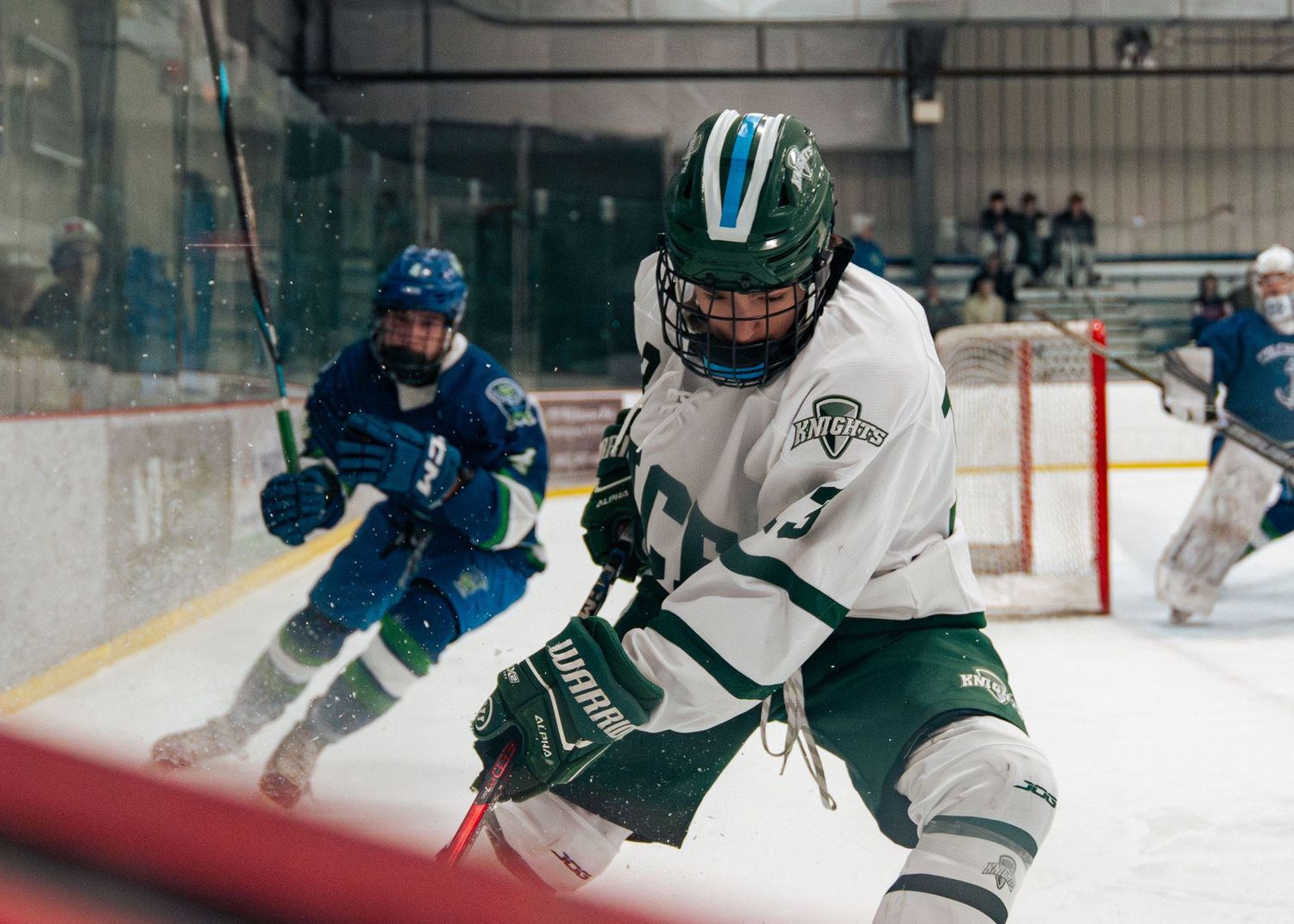 Ice hockey player in white jersey makes a defensive play against opponent in teal during competitive game.