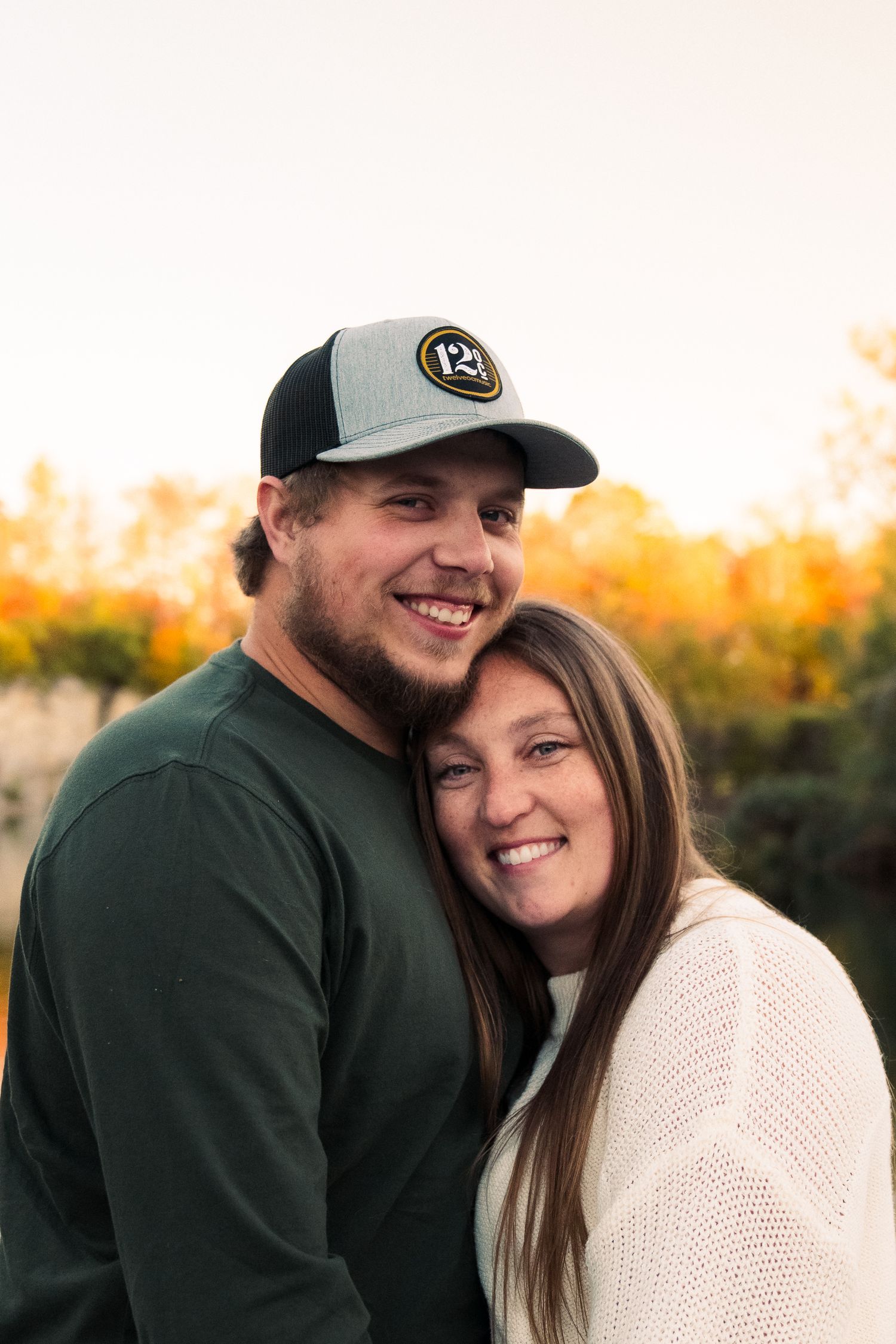 Couple in casual winter attire embracing and laughing during golden hour sunset photo session.