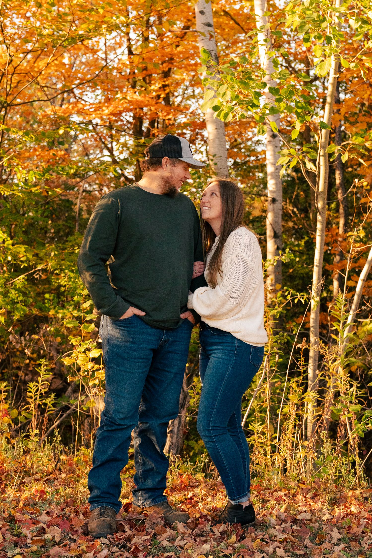 A couple shares romantic moments in a fall forest setting with vibrant orange and yellow autumn foliage.