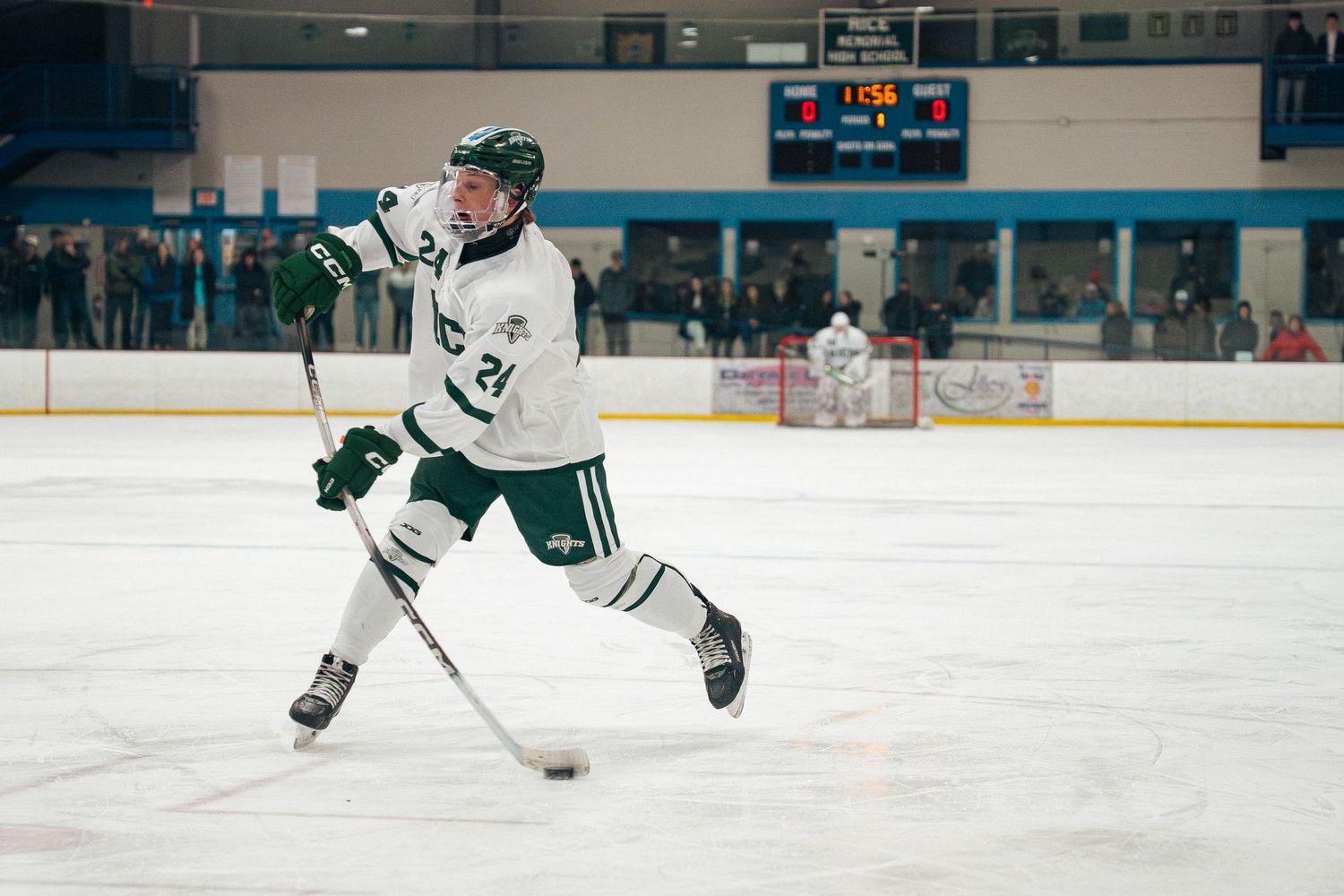 Hockey player in green and white jersey skates across ice rink during game action.
