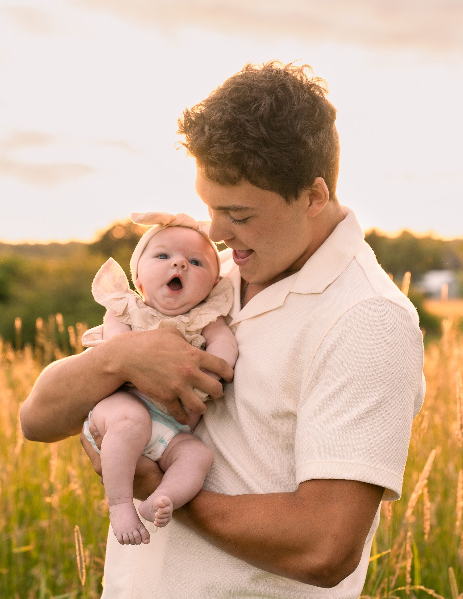 Parents gaze adoringly at their newborn baby in an outdoor setting.
