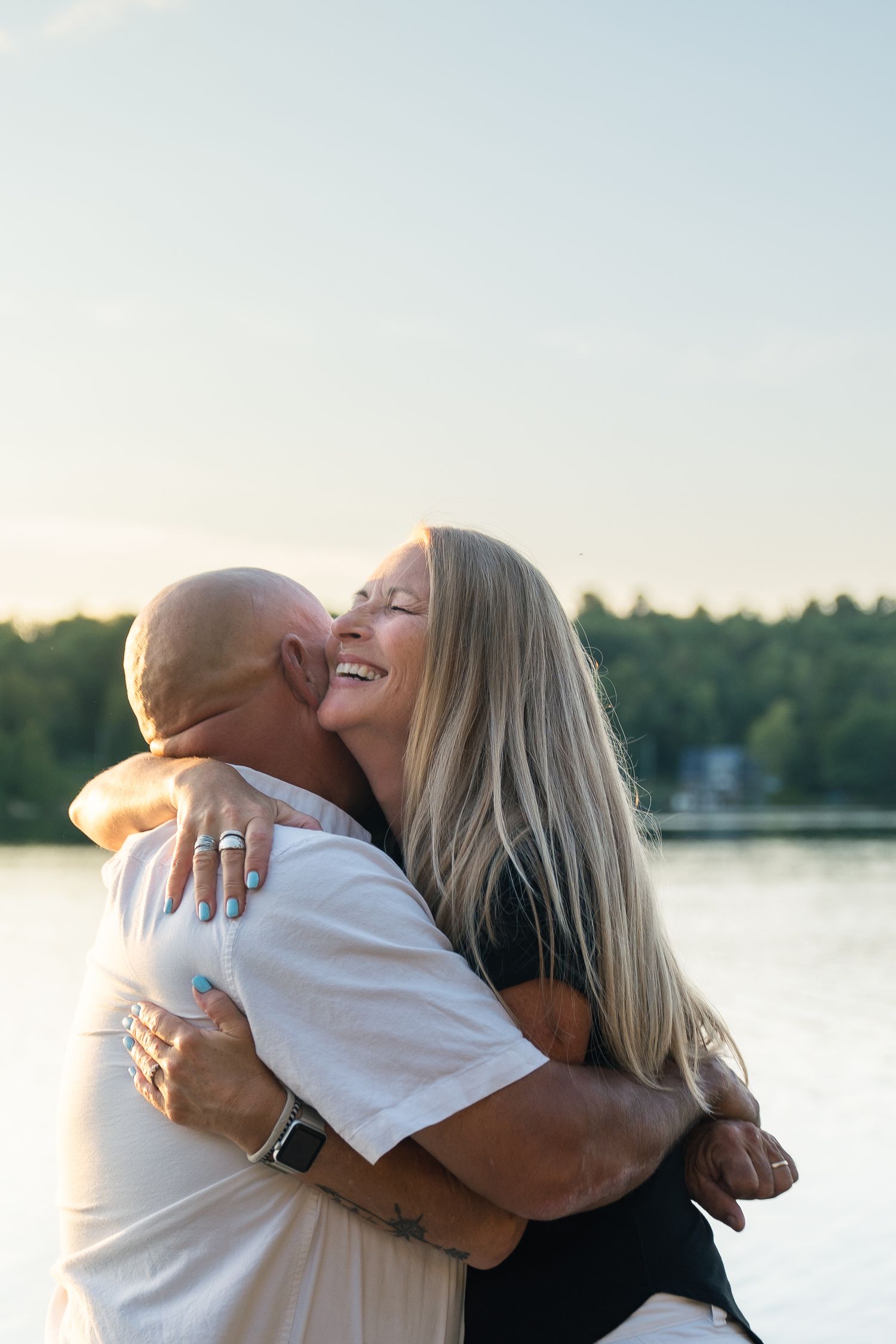 A couple embraces and kisses tenderly by a tranquil lake at sunset.