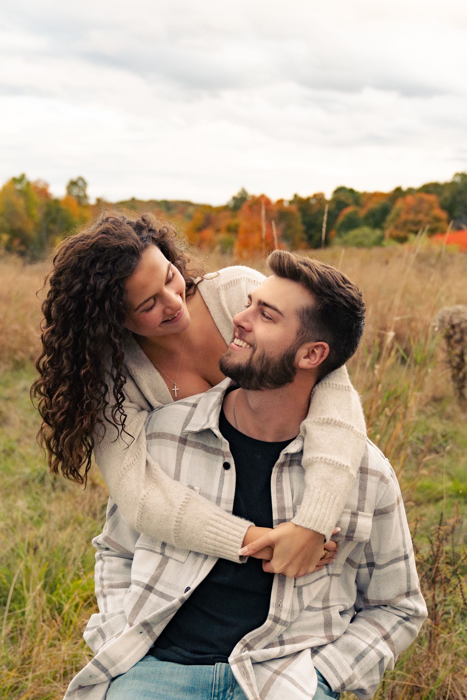 A couple sharing tender moments in a field during autumn with fall foliage in the background.