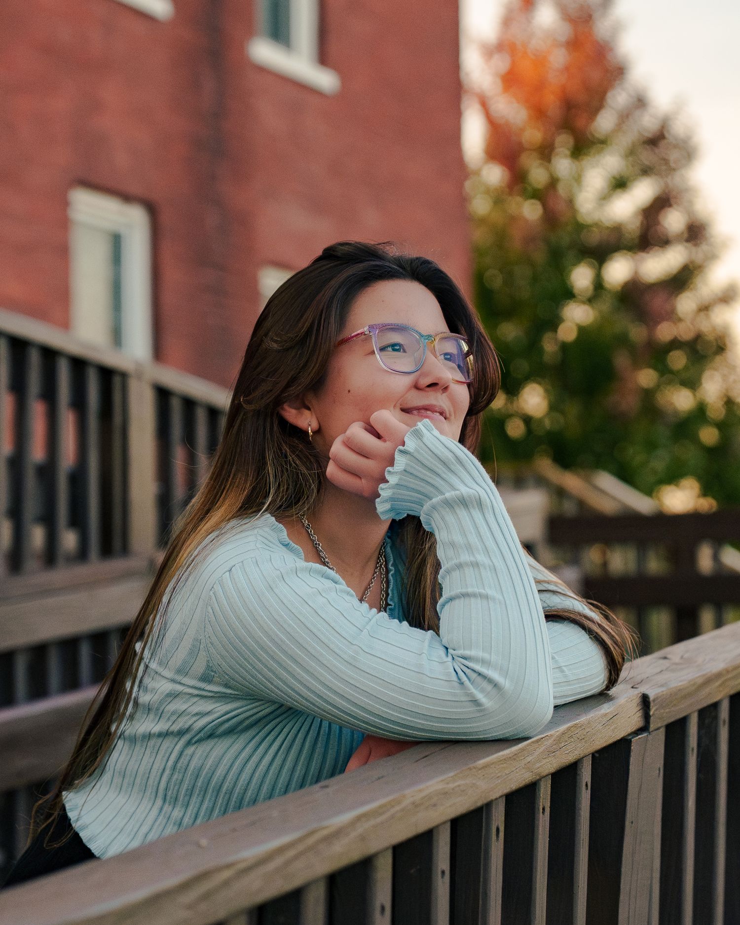 A person in a light blue sweater rests thoughtfully on a wooden railing during golden hour.