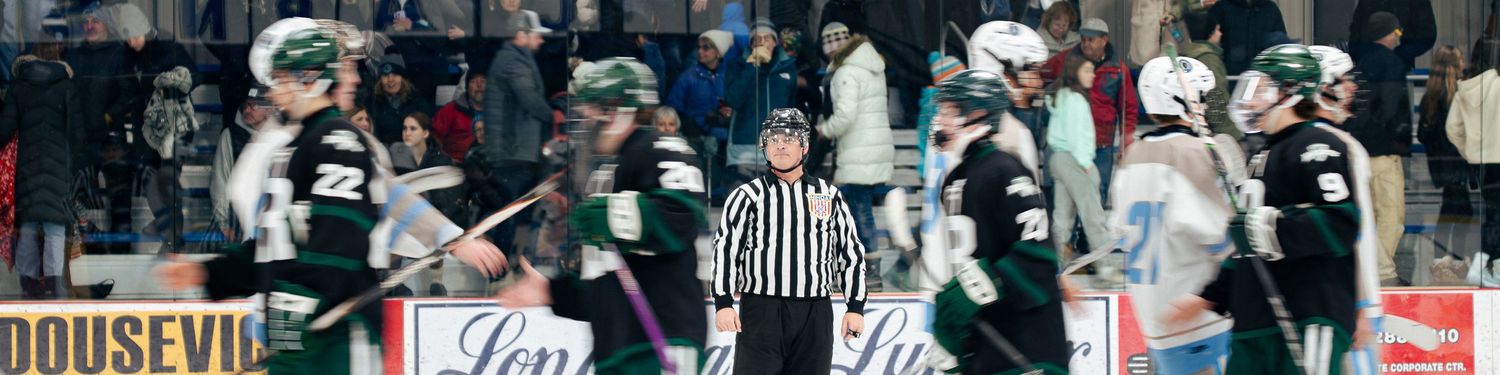 Ice hockey players and officials gather near the boards during a game with advertisements visible in the background.