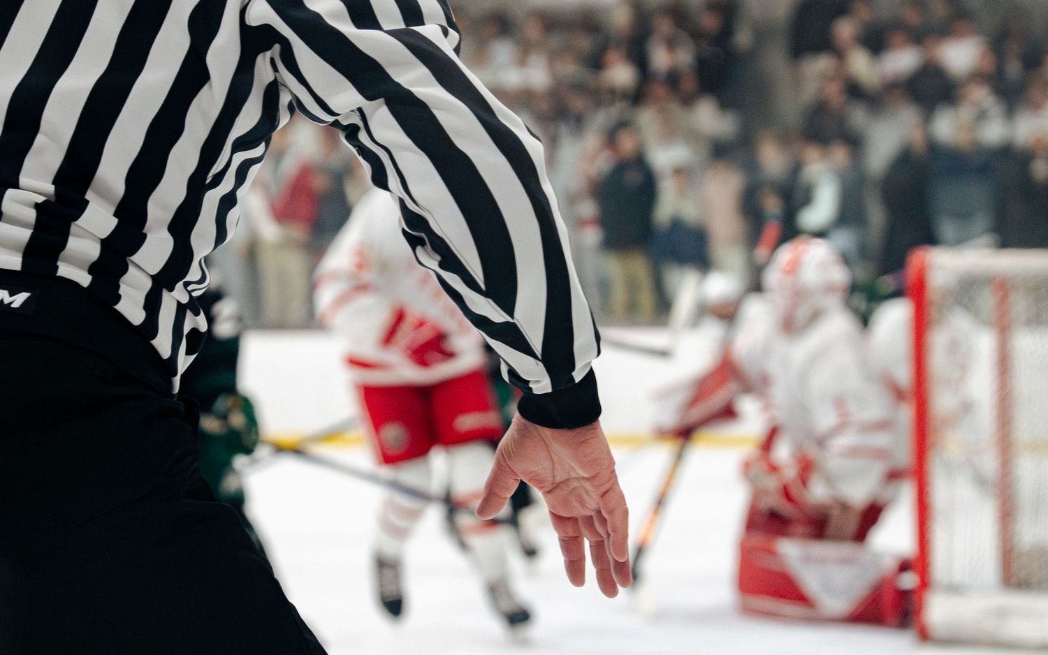 Hockey officials in striped uniforms gather on the ice during a professional game with players in the background.