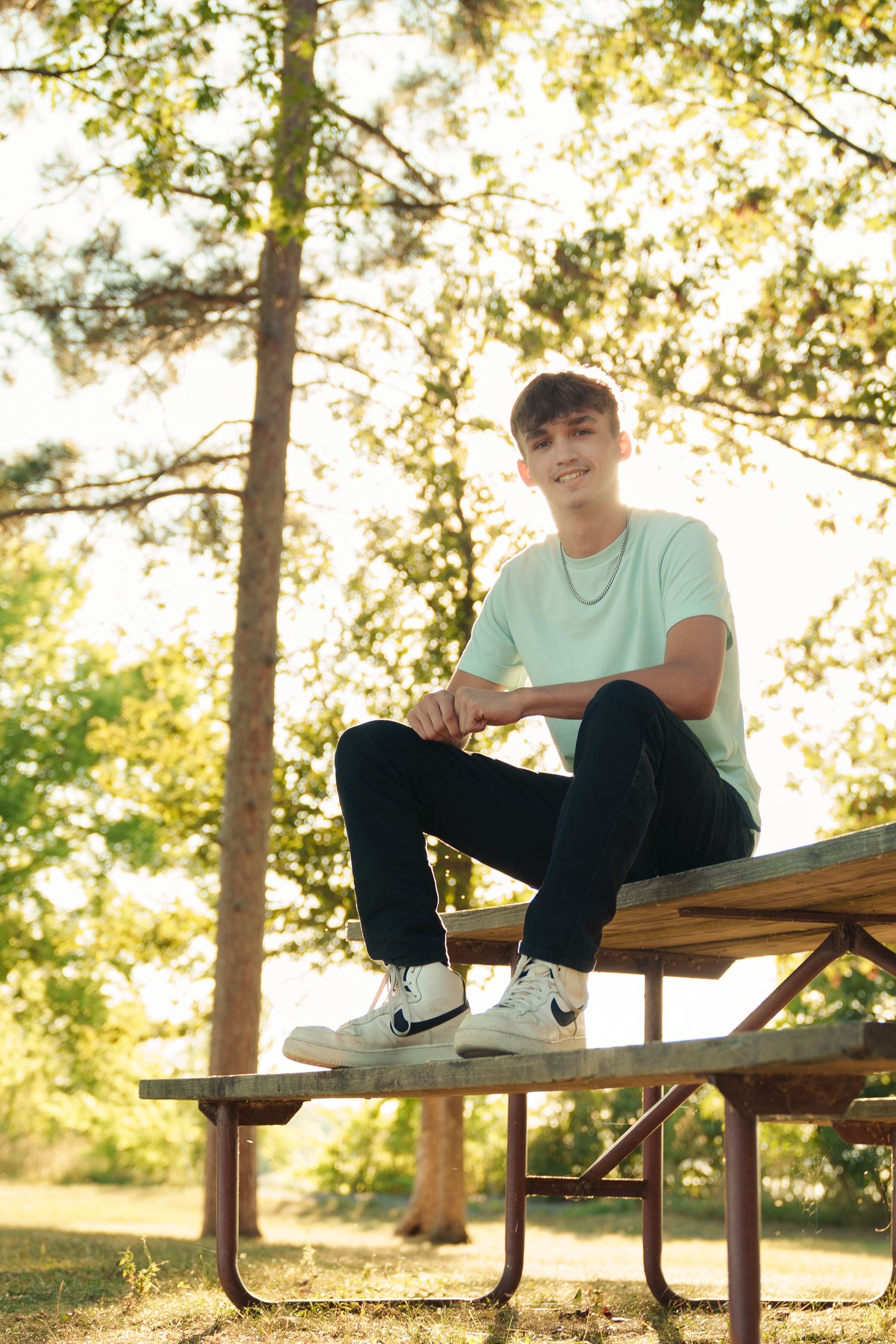 Casual poses on a wooden picnic table in a sunlit park setting.
