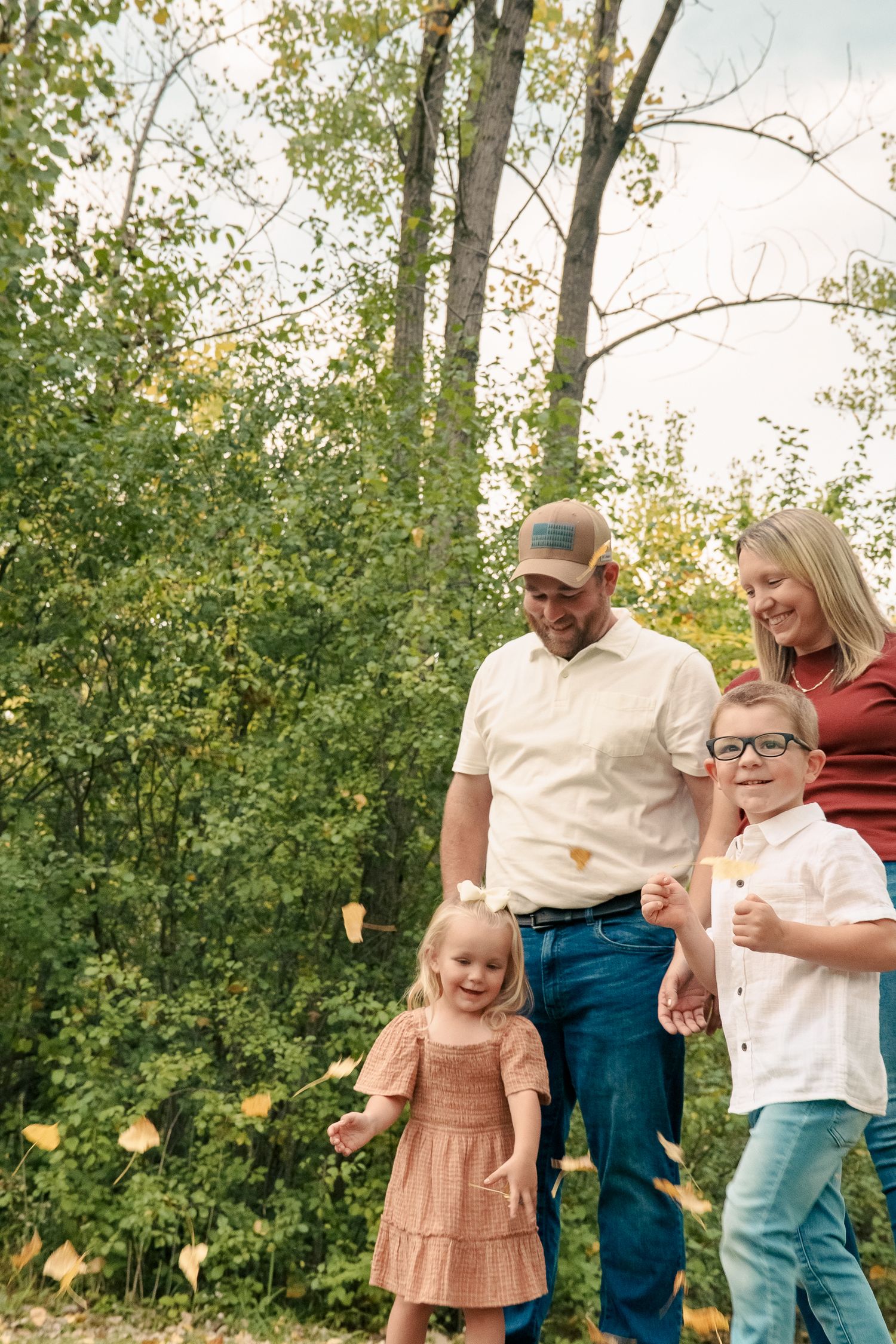 A family shares joyful moments together outdoors during a fall photo session among trees and natural scenery.