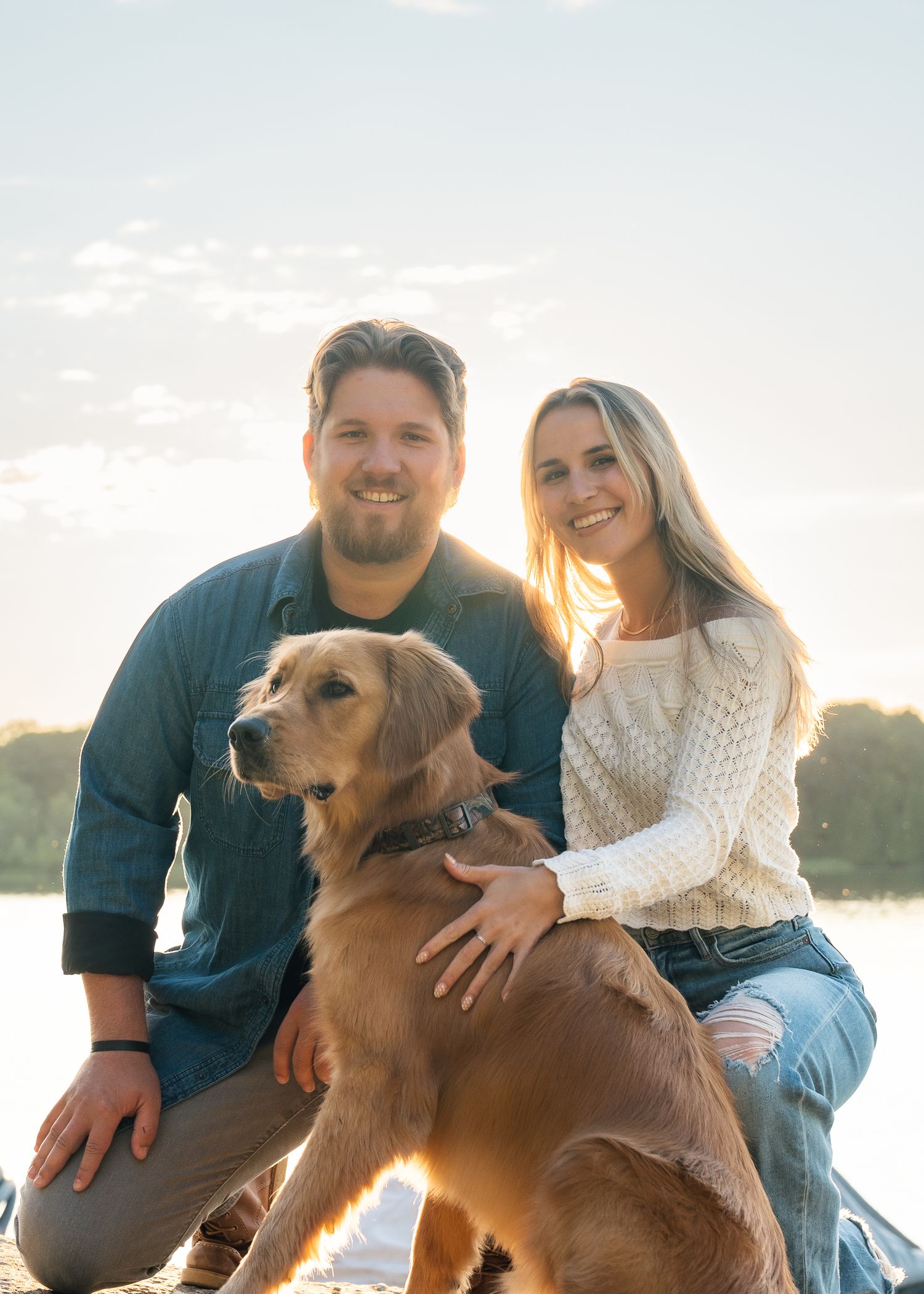 A couple sits outdoors with their golden retriever dog during golden hour sunset in a casual photoshoot.