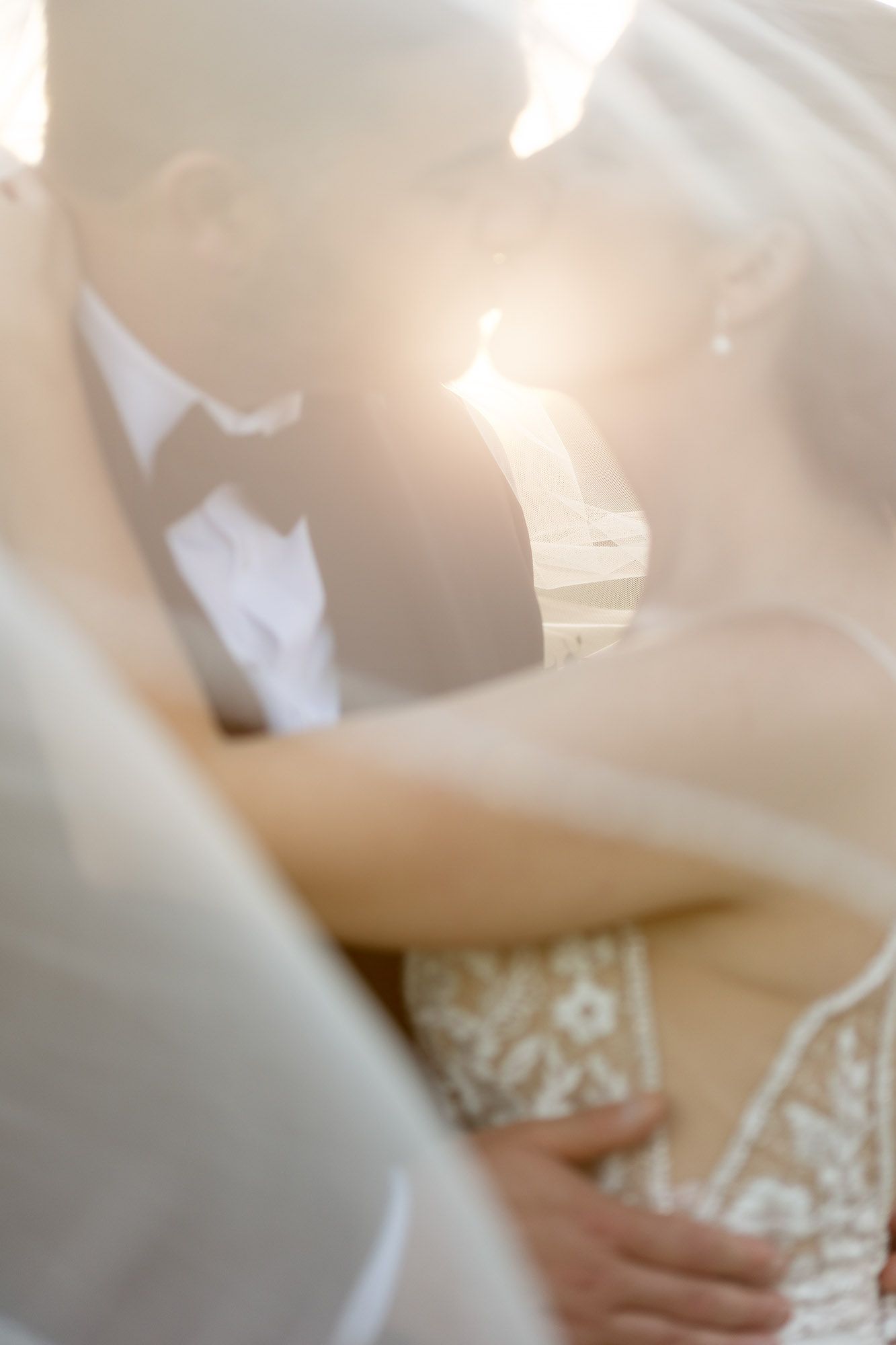 Bride and groom kissing in the sun covered in veil. Albany NY wedding