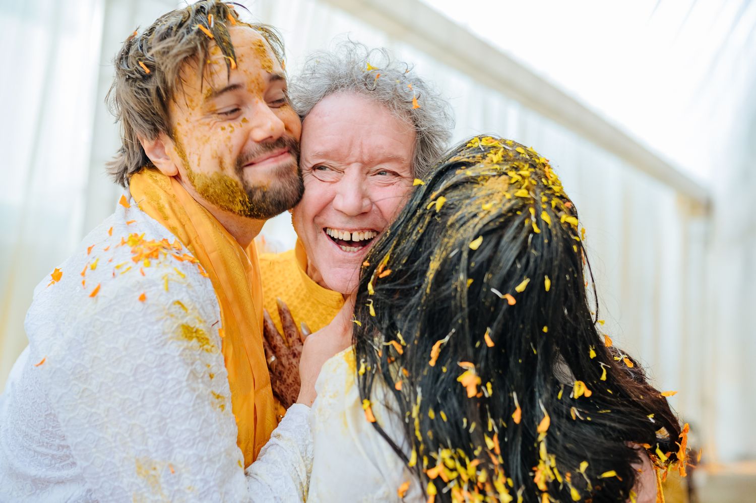 Bride and groom covered in turmeric during an Indo-Norwegian wedding and Family applying Haldi to the bride during a joyful wedding ritual