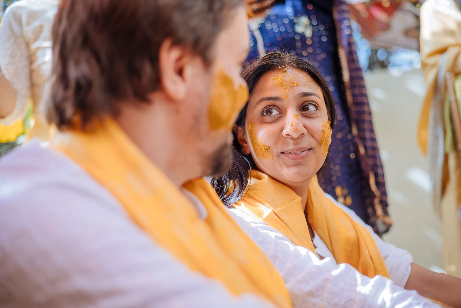 Bride and groom covered in turmeric during an Indo-Norwegian wedding and Family applying Haldi to the bride during a joyful wedding ritual