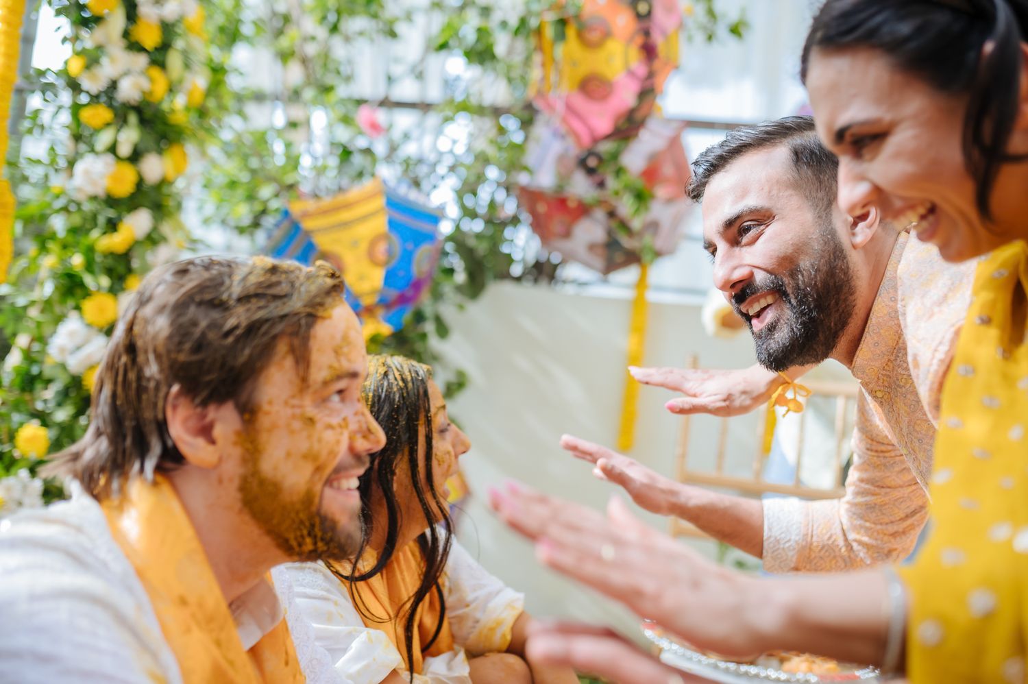 Bride and groom covered in turmeric during an Indo-Norwegian wedding and Family applying Haldi to the bride during a joyful wedding ritual