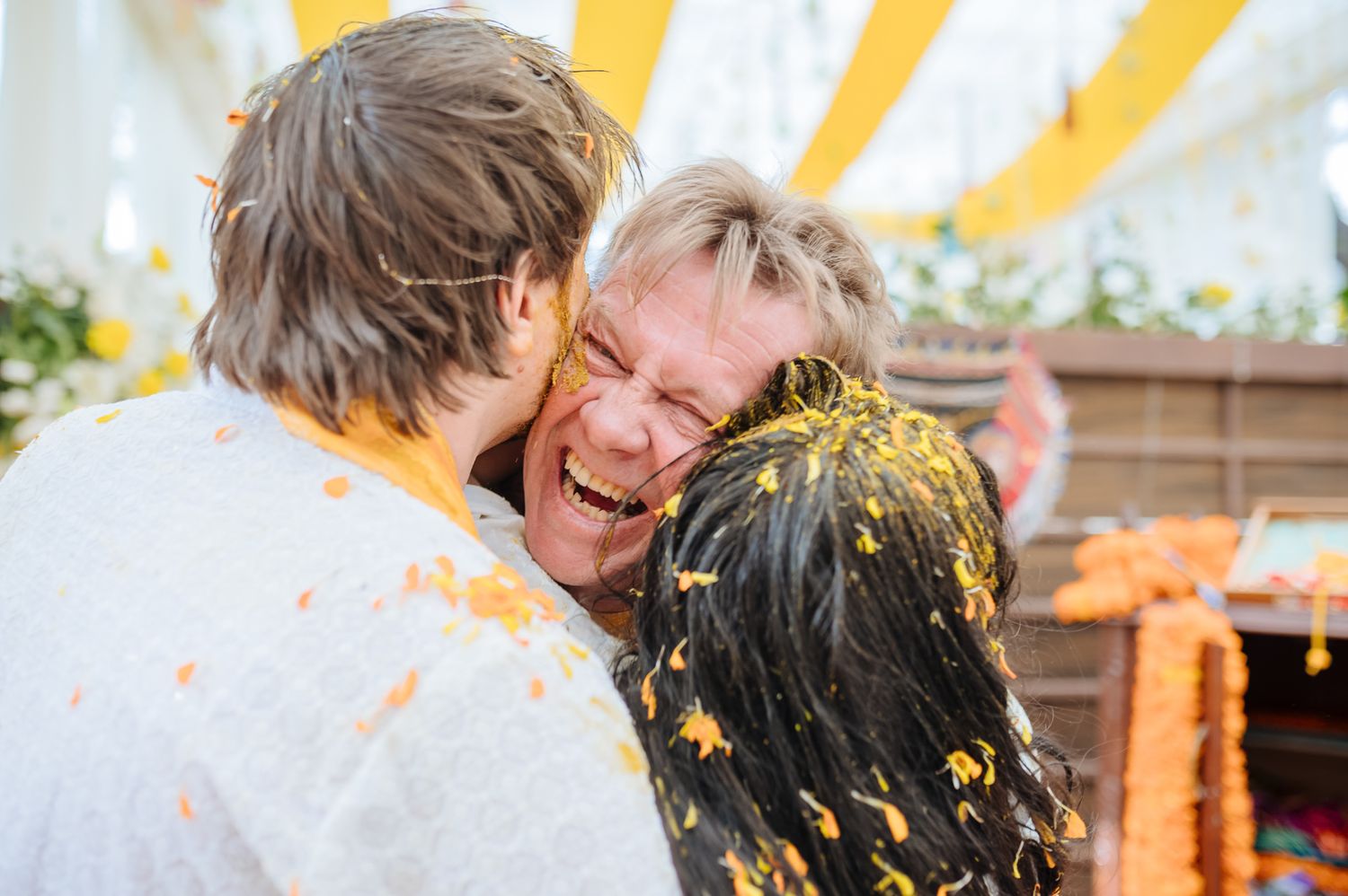 Bride and groom covered in turmeric during an Indo-Norwegian wedding and Family applying Haldi to the bride during a joyful wedding ritual